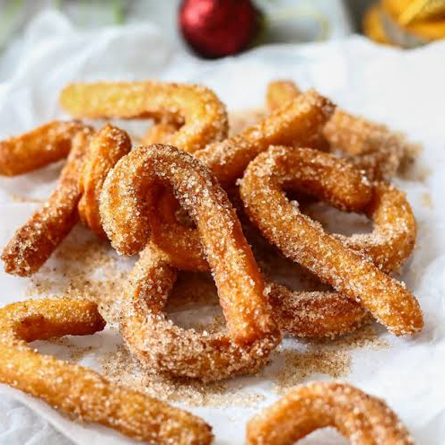 A plate of freshly fried churros coated in cinnamon sugar, shaped in curved forms, with a festive ambiance.